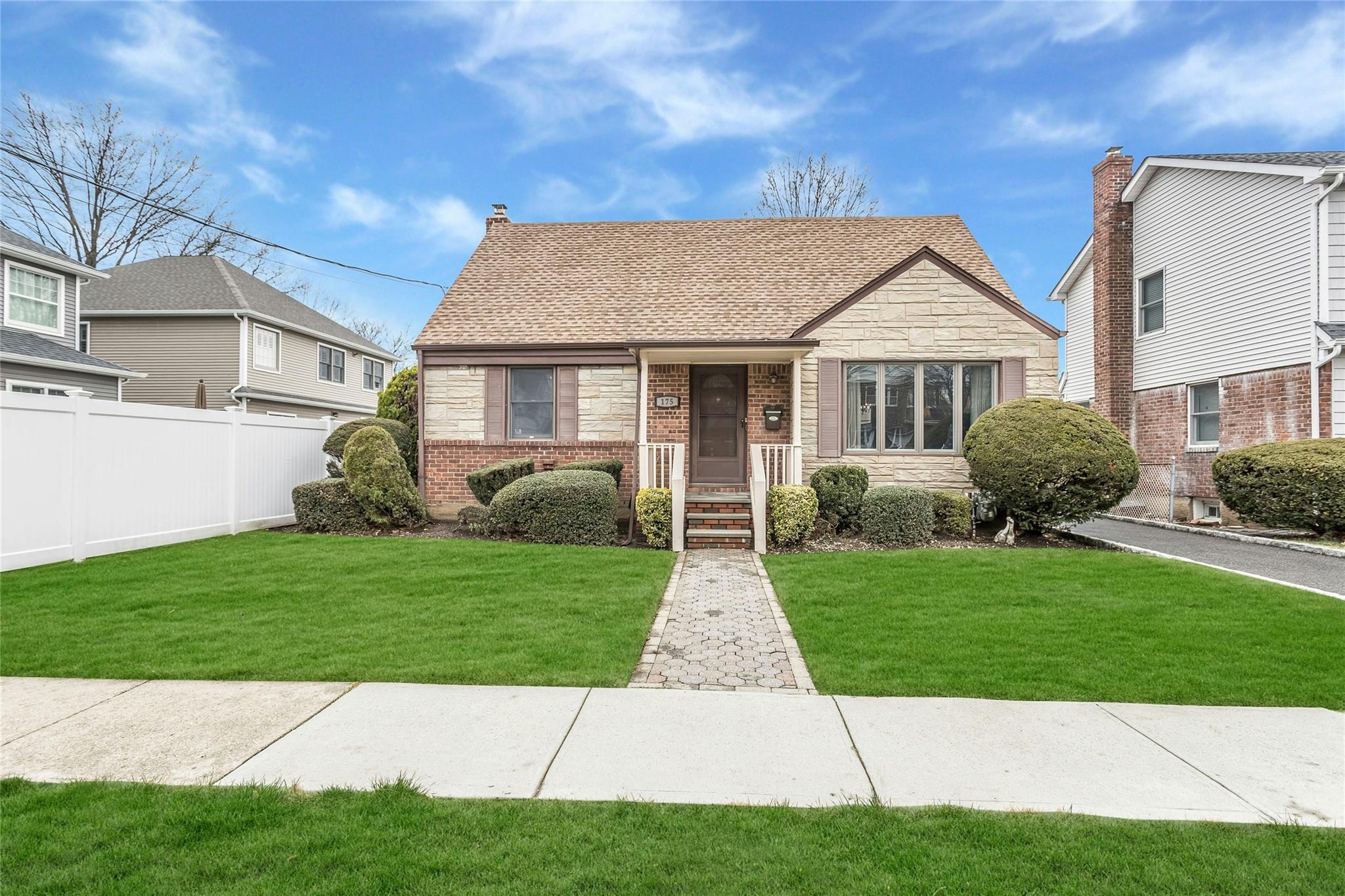 Cape with a shingled roof, a front yard, fence, and stone siding