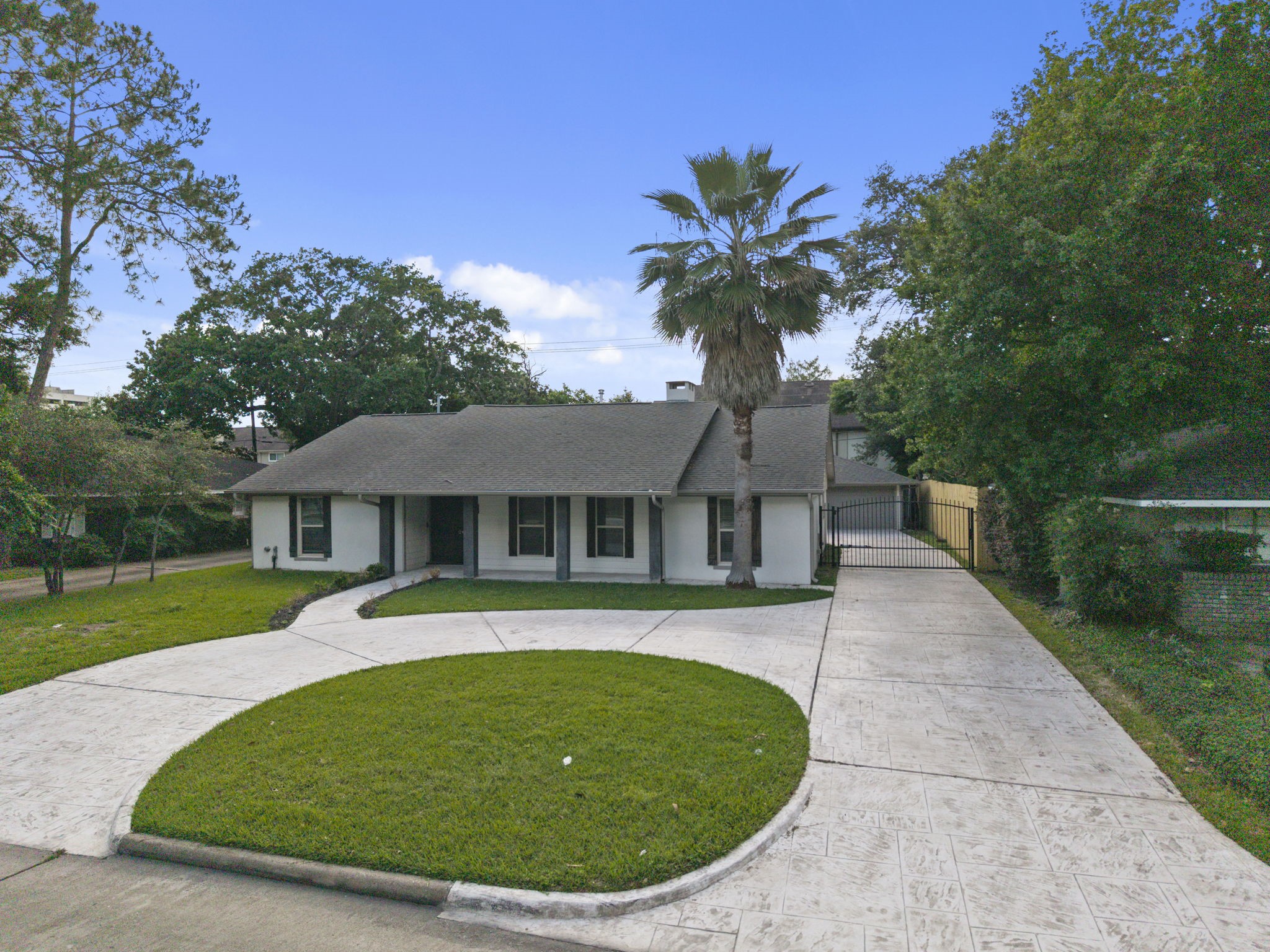 2402 Chimney Rock Road Houston, TX 77057 - Photo 3 of 36 Beautifully maintained home featuring a stamped concrete driveway and gated entrance. Mature trees provide privacy, complemented by a well-kept yard in a quiet neighborhood.