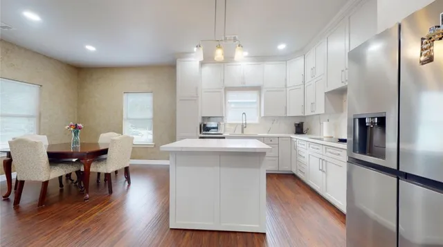 a kitchen with stainless steel appliances a dining table chairs a sink dishwasher a refrigerator and microwave with wooden floor