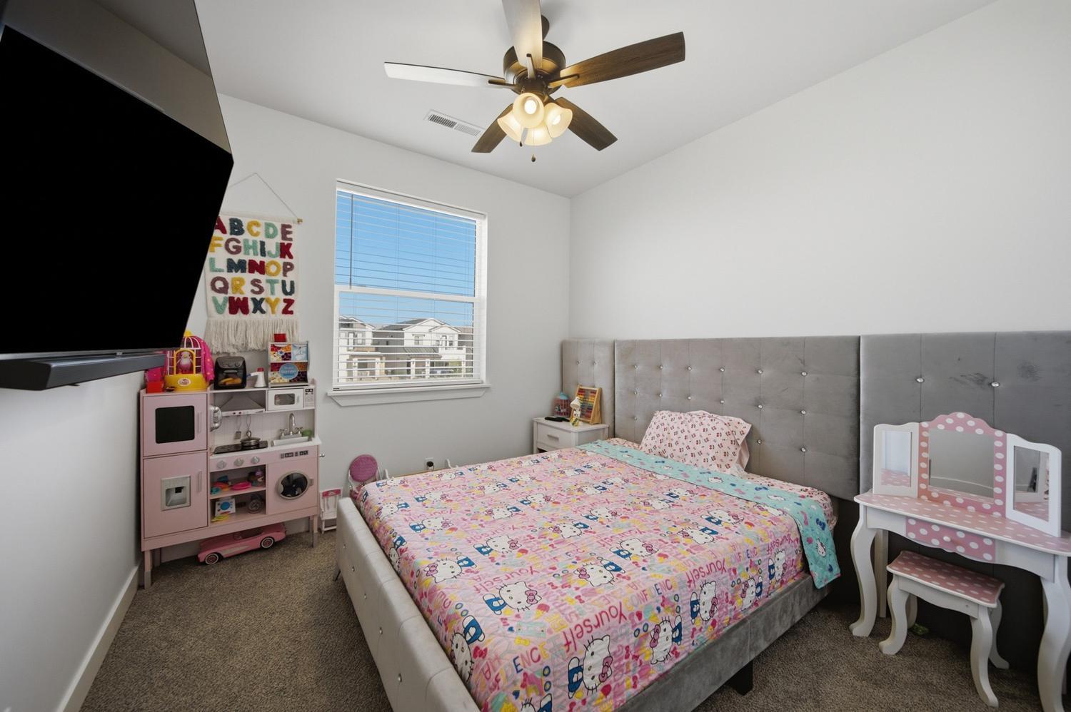6144 Red Sand Lane St. George, UT 84790 - Photo 13 of 19 Playful and bright, this bedroom features a plush upholstered bed, a whimsical alphabet garland, and a dedicated play-kitchen corner for imaginative fun. A mini vanity with stool adds a sweet finishing touch, proving this home has charm for family members of every age.