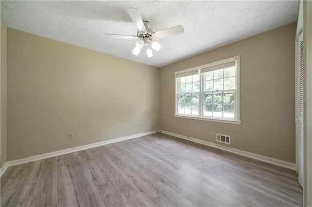 an empty room with wooden floor fan and windows