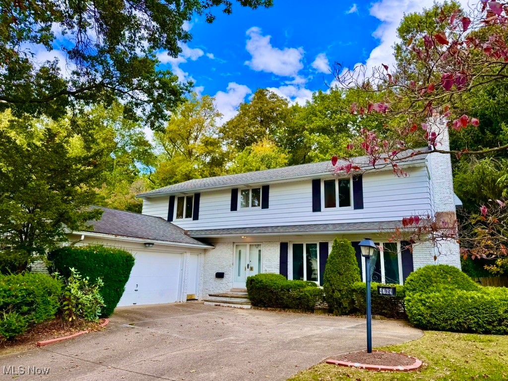 Traditional home with brick siding, driveway, a garage, a shingled roof, and a chimney