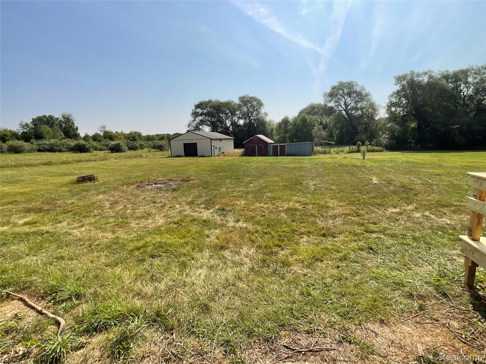 10119 Godfrey Road Bancroft, MI 48414 - Photo 32 of 47 Expansive grassy area featuring a white storage building, a red storage shed, and mature trees in the background