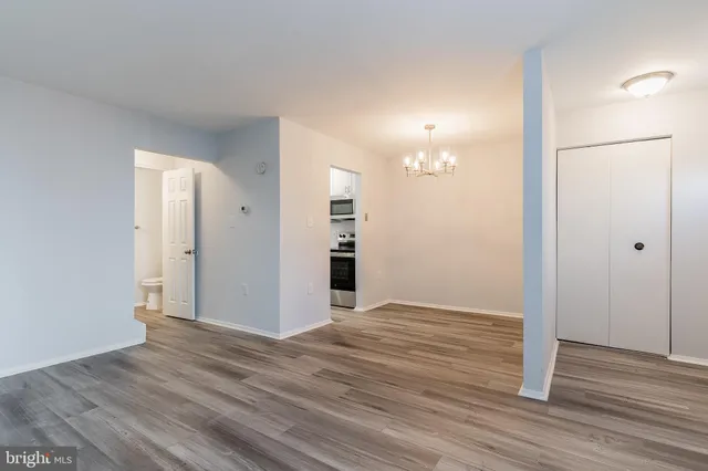 an empty room with wooden floor and way to kitchen