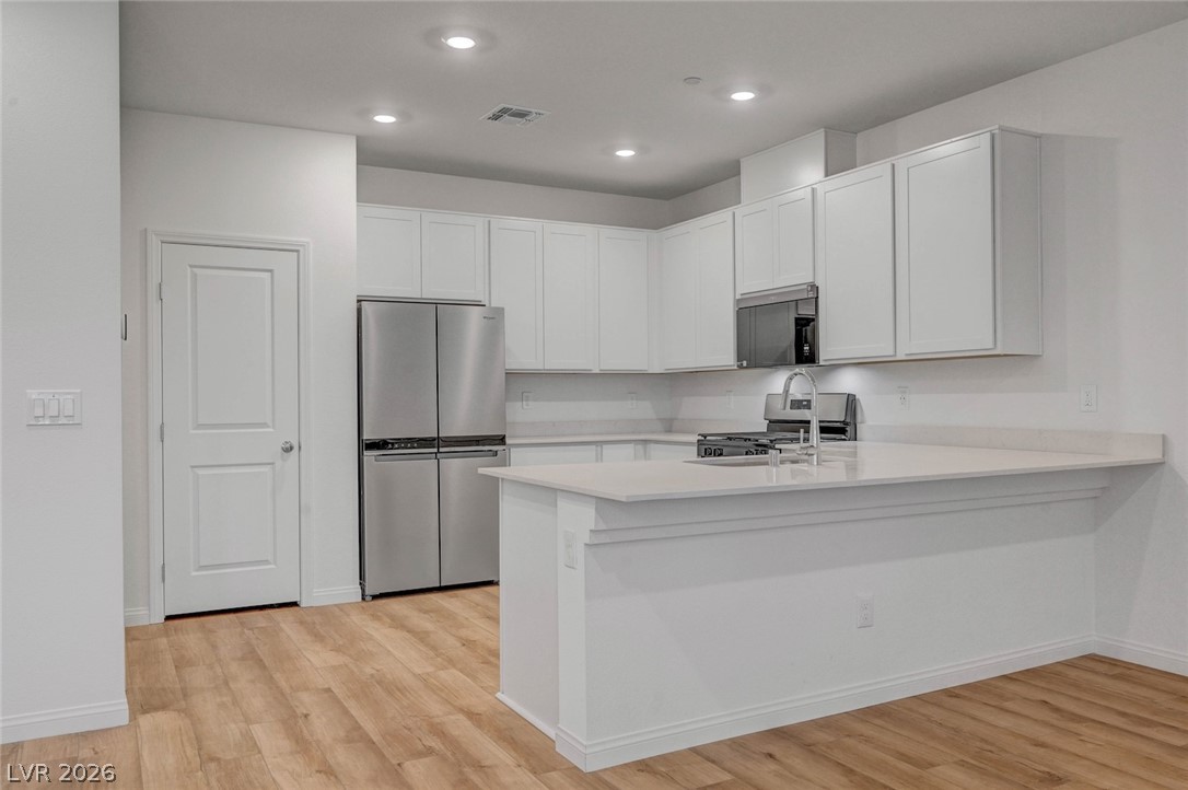 3548 Dimora Street Henderson, NV 89044 - Photo 15 of 40 Kitchen with light wood finished floors, stainless steel appliances, light countertops, visible vents, and a peninsula
