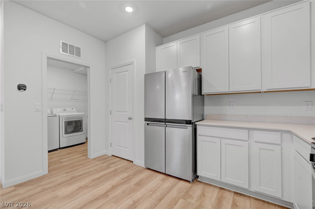 3548 Dimora Street Henderson, NV 89044 - Photo 19 of 40 Kitchen featuring visible vents, freestanding refrigerator, light wood finished floors, and white cabinets