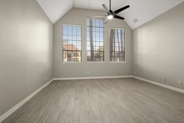 an empty room with wooden floor ceiling fan and windows