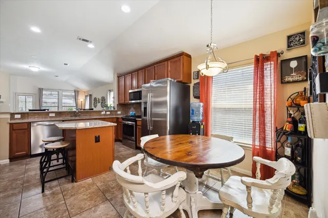 a kitchen with stainless steel appliances granite countertop a refrigerator a stove a sink a dining table and chairs