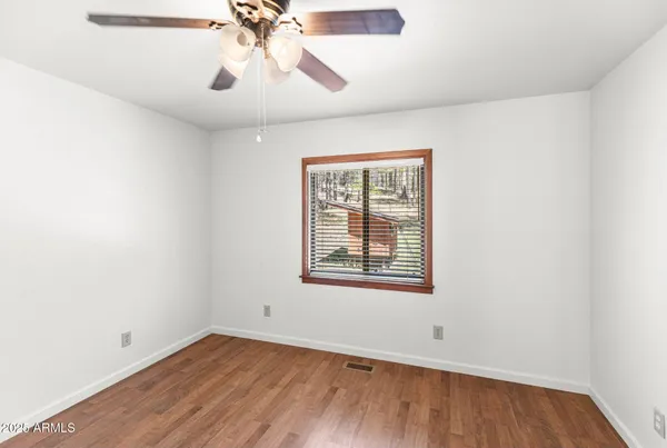 an empty room with wooden floor chandelier fan and windows