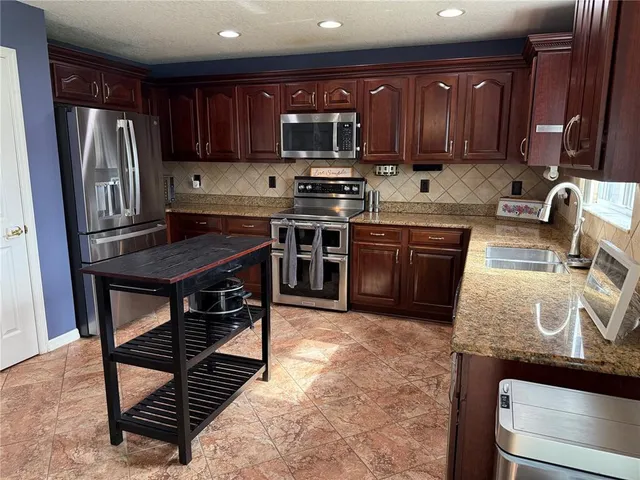a kitchen with stainless steel appliances granite countertop a stove top oven a sink and a refrigerator