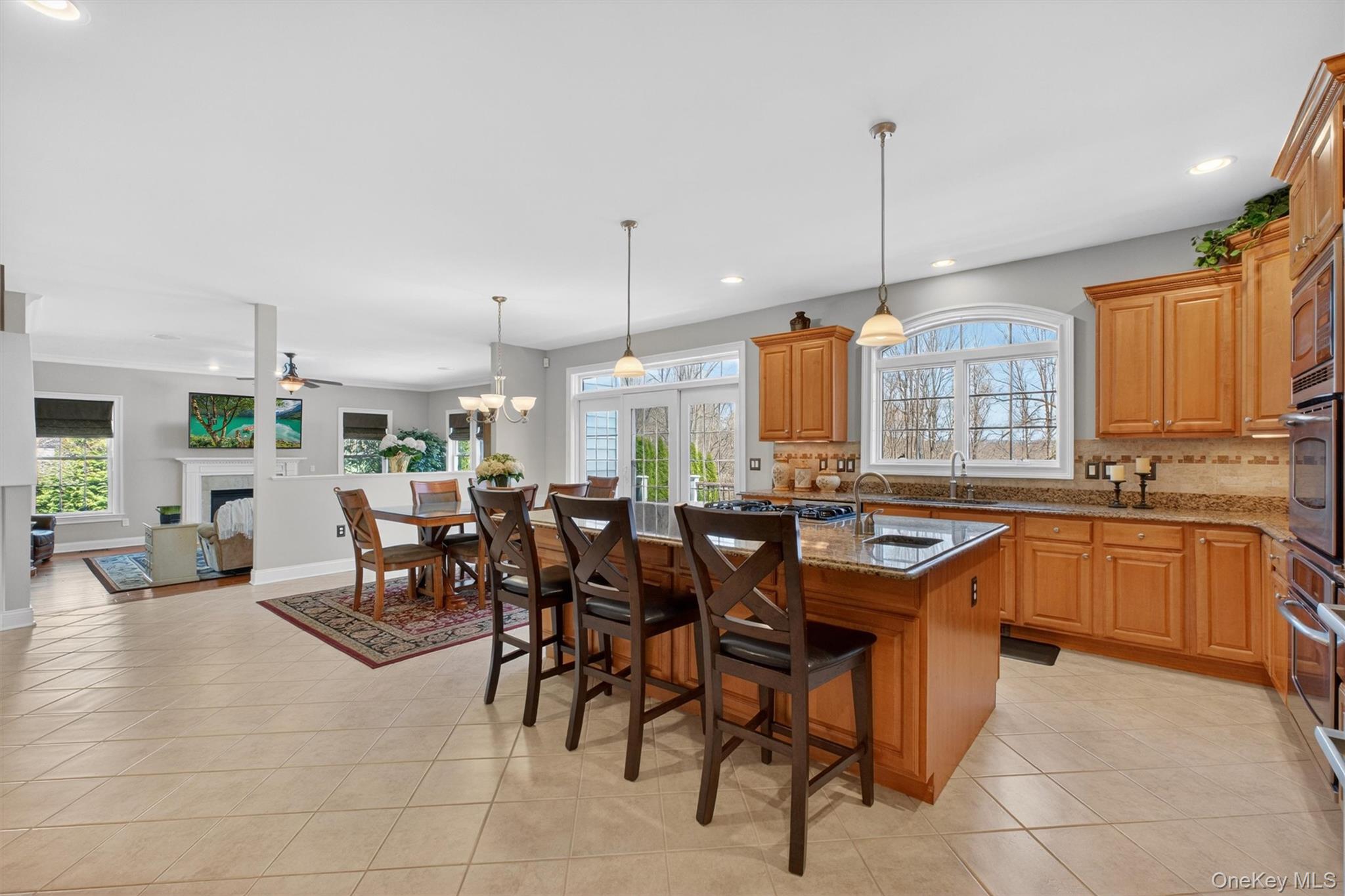 196 Country Club Road Hopewell Junction, NY 12533 - Photo 10 of 50 This stunning kitchen is a true showpiece and an entertainer’s dream, seamlessly blending elegance with everyday functionality. Durable horizontal tile flooring flows throughout the expansive open-concept space, while abundant recessed lighting illuminates every detail. At the heart of the kitchen is an impressive, oversized center island, crowned with luxurious Giallo Pallia granite featuring a refined ogee edge and generous overhang for seating. Complete with a 36-inch five-burner gas cooktop and prep sink, the island comfortably accommodates four, creating the perfect gathering place for casual dining, conversation, and effortless meal preparation. Rich, warm-toned cabinetry surrounds the space, offering exceptional storage and timeless style, beautifully accented by sleek silver hardware and a stone-style ceramic backsplash finished with an elegant accent border.