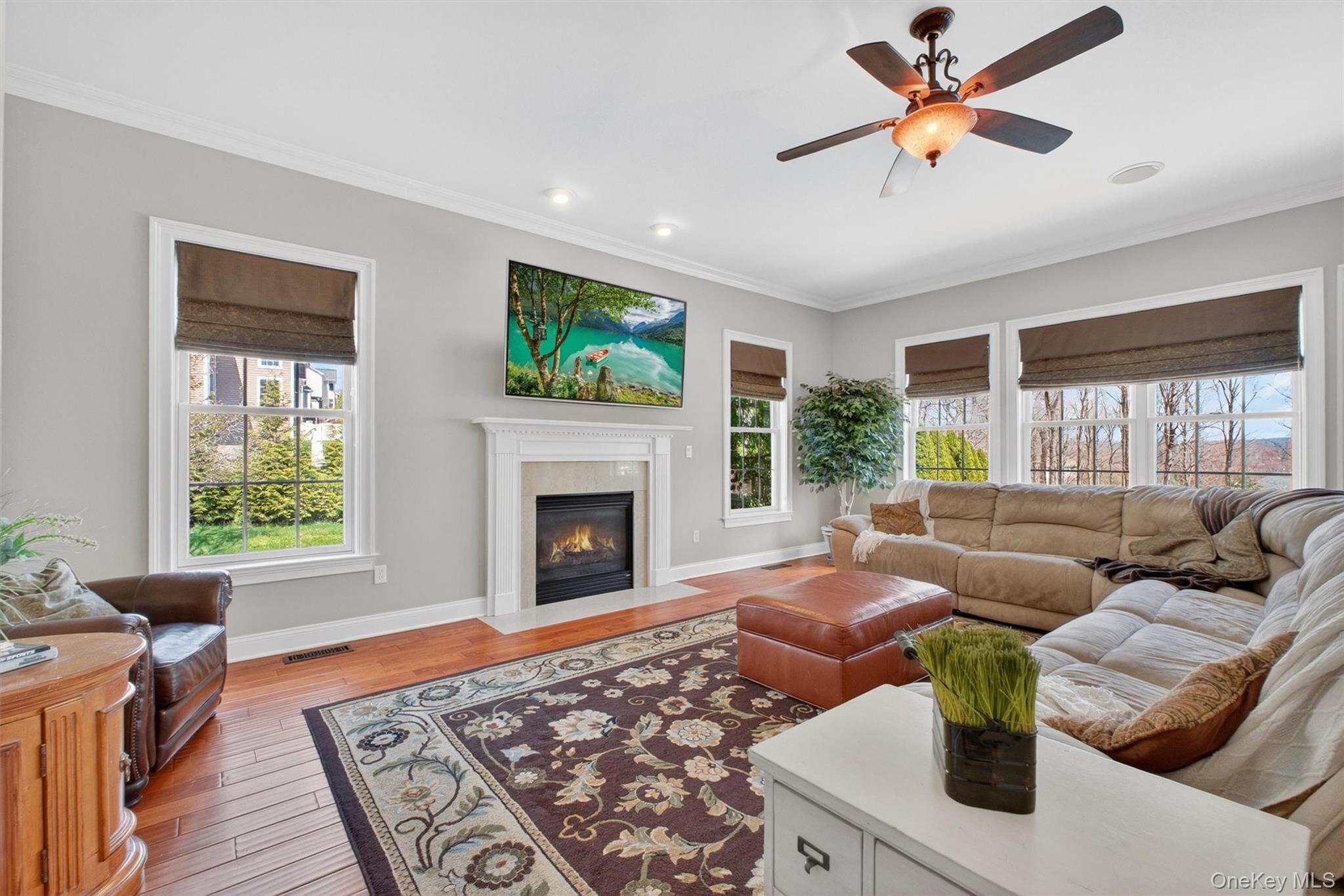 196 Country Club Road Hopewell Junction, NY 12533 - Photo 12 of 50 The spectacular family room is a grand yet inviting space, defined by soaring ceilings and an impressive sense of scale. At its center, a stunning 36-inch gas fireplace is showcased by a custom marble hearth and an elegant, oversized mantel, richly detailed to reflect the exceptional craftsmanship and sophistication found throughout the home. Accent lighting, including recessed and directional eyeball lighting, highlights this dramatic focal point, while built-in surround sound speakers create the perfect atmosphere for entertaining or relaxing. A magnificent wall of windows dressed in custom fabric shades fills the room with natural light and beautiful views, while gleaming hardwood floors add warmth and timeless style. Spacious enough for large gatherings yet equally suited for cozy evenings at home, this extraordinary family room is the perfect blend of luxury, comfort, and architectural beauty.