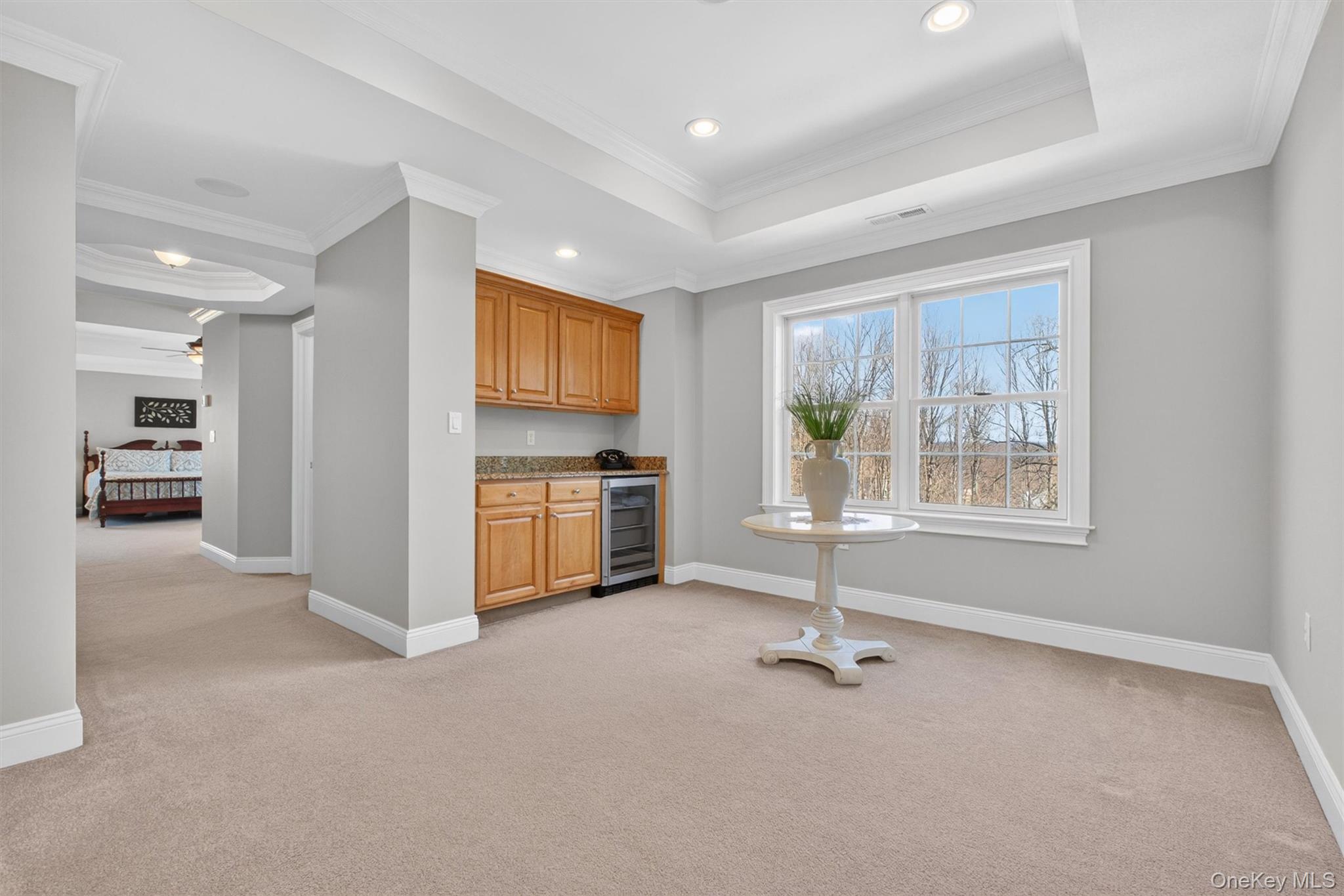 196 Country Club Road Hopewell Junction, NY 12533 - Photo 17 of 50 The luxurious primary suite spans the entire length of the rear of the home, creating a private retreat of truly impressive proportions. Enter through elegant double doors into this remarkable sanctuary, where an oversized 10' x 13' sitting area with a tray ceiling offers the perfect space to unwind. Beautiful custom cabinetry topped with Giallo granite provides both style and convenience, complemented by a GE Monogram beverage refrigerator and recessed lighting. Thoughtfully designed as the perfect place for morning coffee, evening relaxation, or a private retreat within the suite, this exceptional sitting area elevates the primary bedroom to a true resort-like escape.