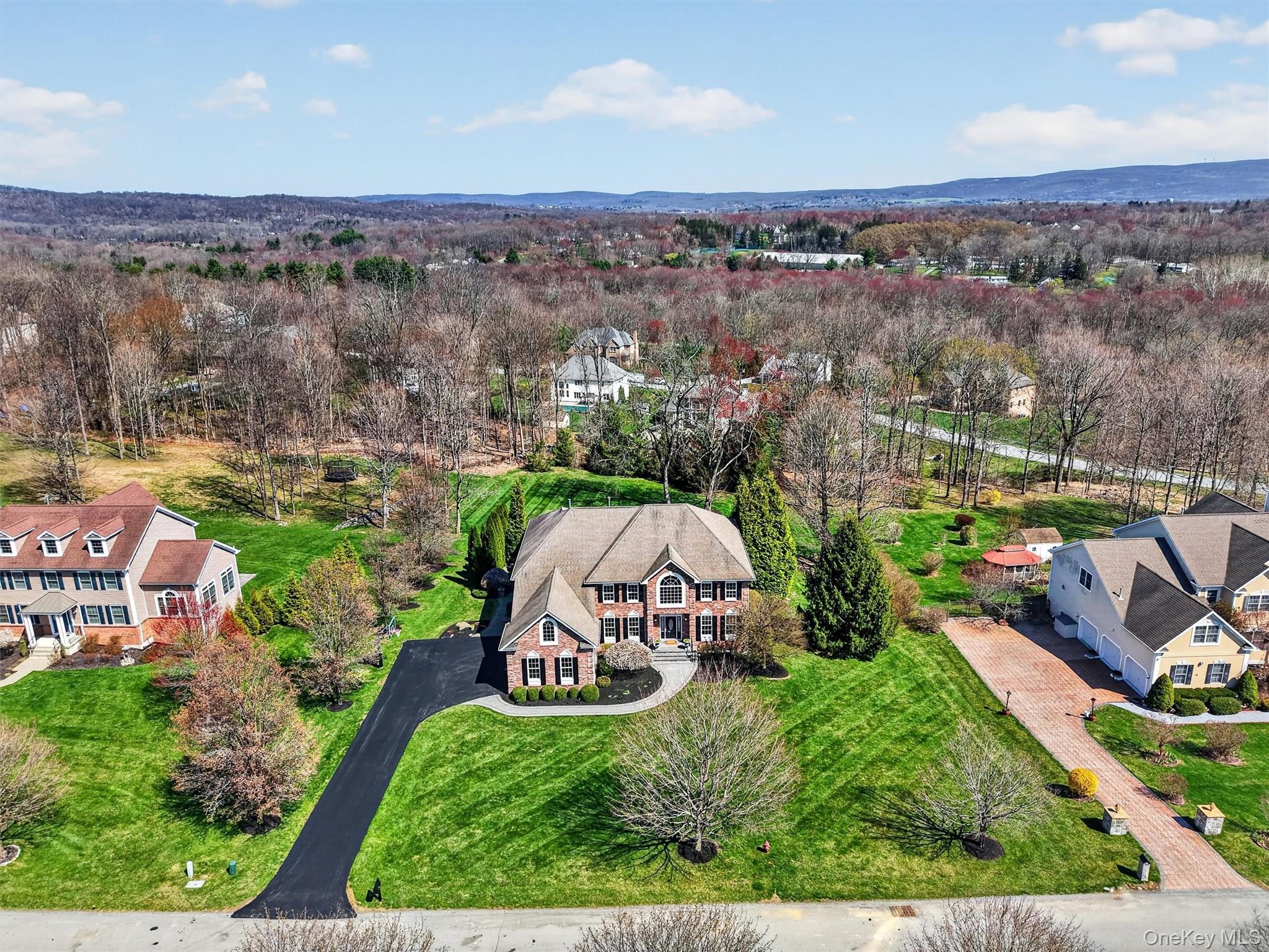 196 Country Club Road Hopewell Junction, NY 12533 - Photo 3 of 50 A stunning aerial side view showcases this beautifully maintained estate home, set on pristine, professionally manicured grounds and surrounded by mature trees that provide exceptional privacy. The expansive, newly paved driveway—elegantly accented with cobblestone pillars—offers parking for 6+ vehicles and leads to a massive three-car garage with abundant storage, featuring new Clopay insulated doors with Lift Master belt-drive openers. New front and rear Unilock walkways create seamless access around the property, enhancing both functionality and curb appeal. Every detail has been thoughtfully updated, completing this exceptional home designed for luxurious living and effortless entertaining.