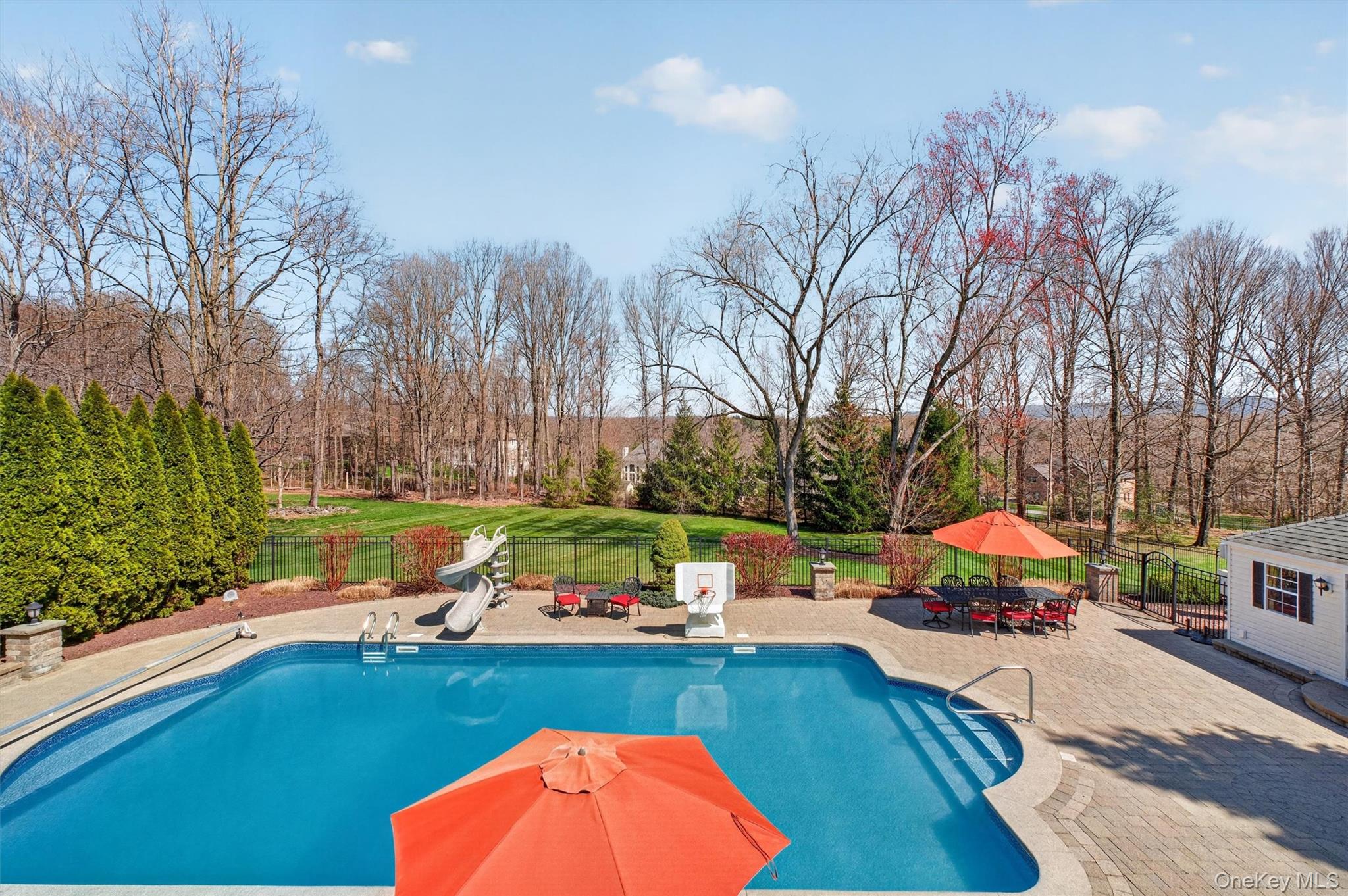 196 Country Club Road Hopewell Junction, NY 12533 - Photo 37 of 50 From the expansive Trex deck, enjoy a breathtaking aerial perspective of your private outdoor oasis, where every detail has been thoughtfully designed for luxury and relaxation. Overlooking the spectacular 22' x 48' in-ground pool—complete with updated systems and resort-style appeal—the view captures the full scale of the beautifully designed patio below. The expansive Unilock paver patio unfolds with multiple entertaining areas, including a custom fire pit, outdoor seating spaces, and seamless flow for gatherings of any size. Beyond the pool, a private, flat rear lawn stretches out—perfect for recreation, play, or simply enjoying the open space—while maintaining a safe and separate area from the pool. Framed by mature trees and set against serene mountain views, this elevated vantage point offers a truly stunning backdrop, blending privacy, nature, and resort-style living into one unforgettable setting