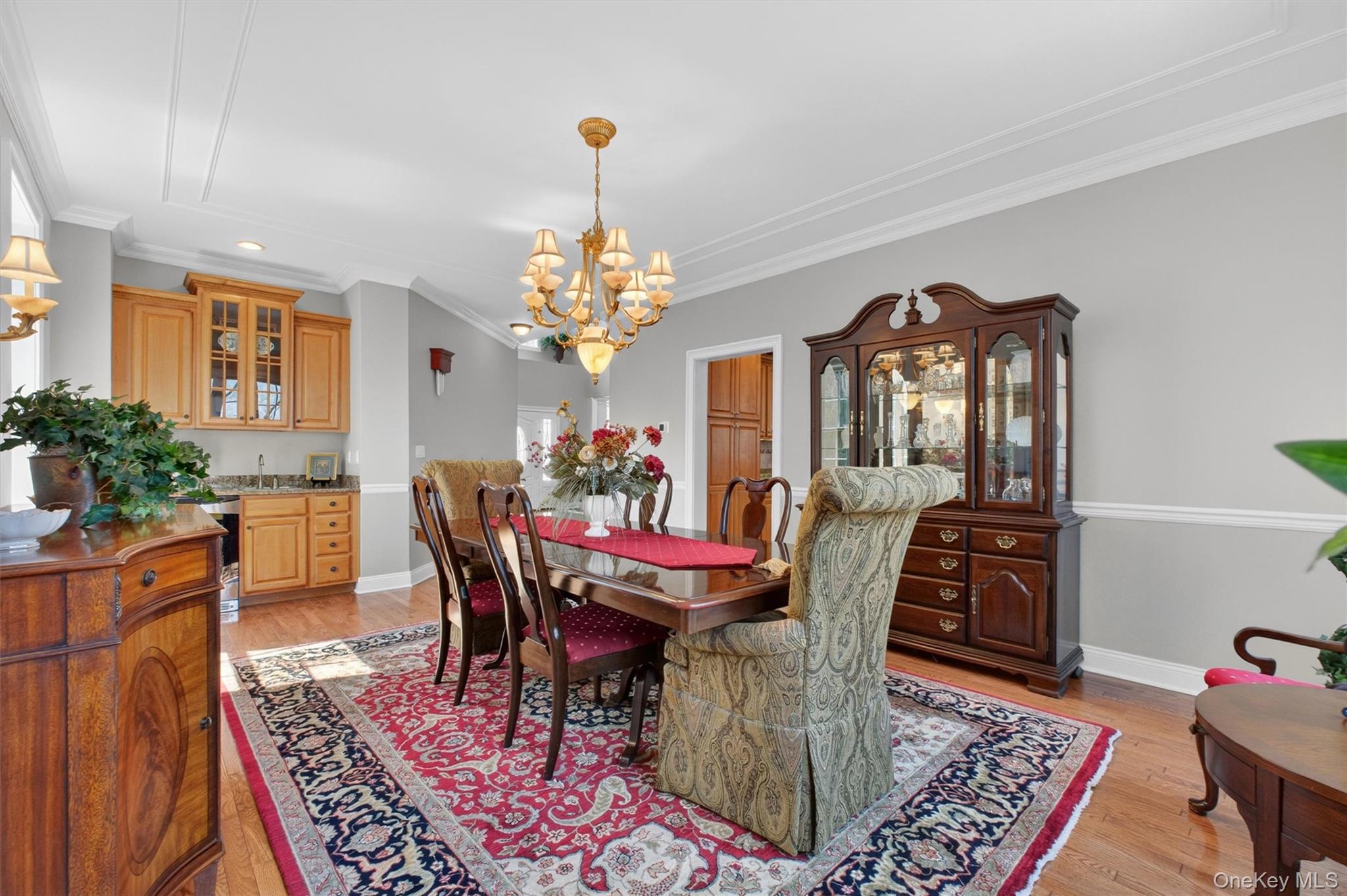 196 Country Club Road Hopewell Junction, NY 12533 - Photo 7 of 50 The grand and gracious dining room is a true showpiece, radiating elegance and warmth from the moment you enter. A wall of oversized windows floods the room with natural light and captures serene treetop views, while exquisite molding, chair rail, and crown molding add timeless sophistication. Remarkably spacious, this stunning room easily accommodates an oversized dining table for large gatherings along with multiple buffets, sideboards, and additional furnishings, all while maintaining an open, airy feel with room for the whole family. Designed for effortless entertaining, it also features a beautifully appointed serving area with a generous 5’ wet sink, custom cabinetry, gleaming granite countertops, a GE wine refrigerator, and generous prep and serving space, all perfectly positioned adjacent to the kitchen for seamless hosting.