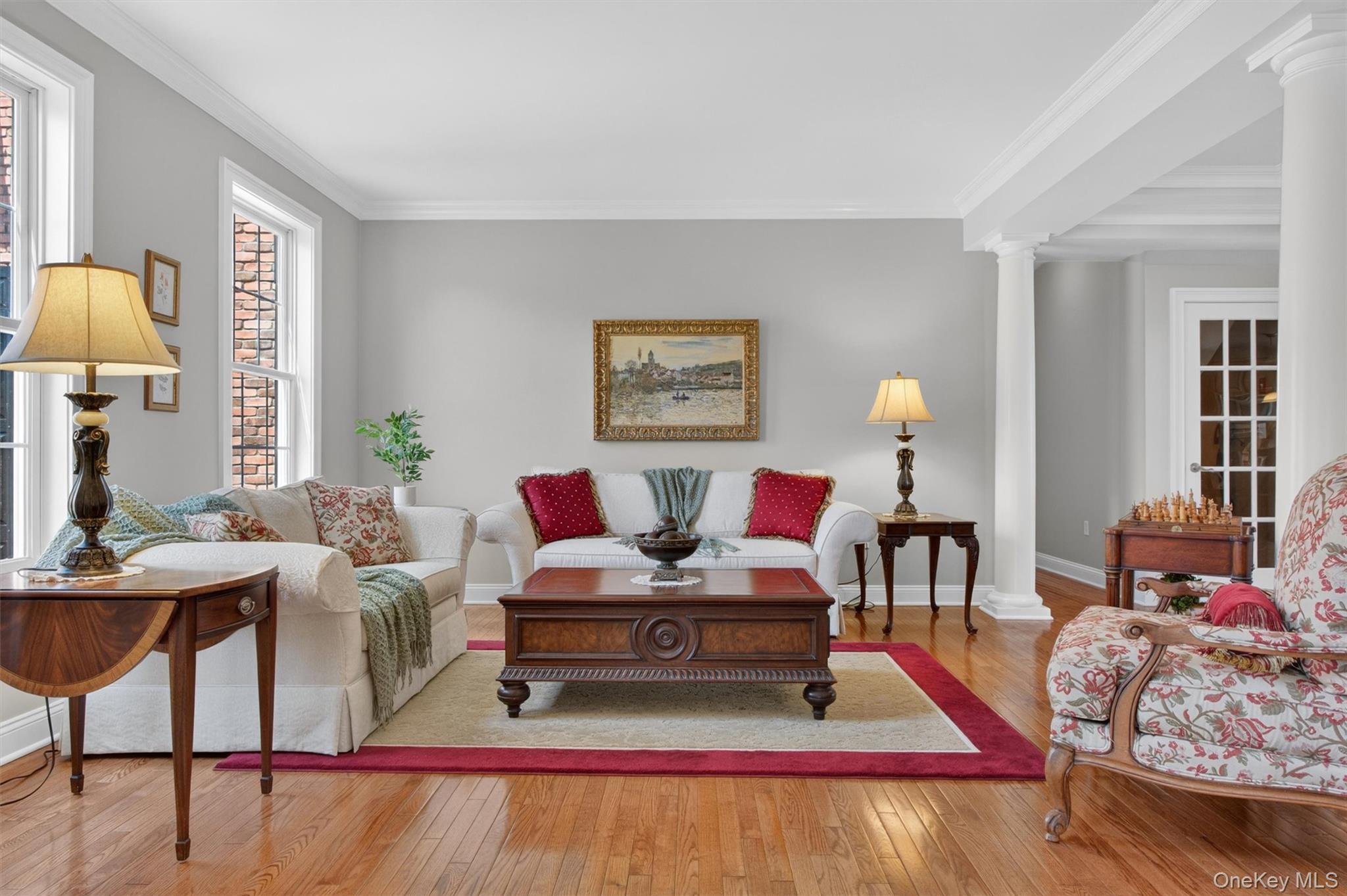 196 Country Club Road Hopewell Junction, NY 12533 - Photo 9 of 50 This elegant formal living room is a beautiful blend of timeless design and refined comfort, anchored by striking architectural columns that define the space while maintaining an open, airy feel. Rich hardwood floors flow seamlessly throughout, adding warmth and sophistication, while a stunning pair of floor-to-ceiling windows fills the room with natural light and enhances the inviting ambiance. Thoughtfully designed for both intimate gatherings and gracious entertaining, this space offers classic charm with a sense of openness that connects effortlessly to the surrounding areas of the home.