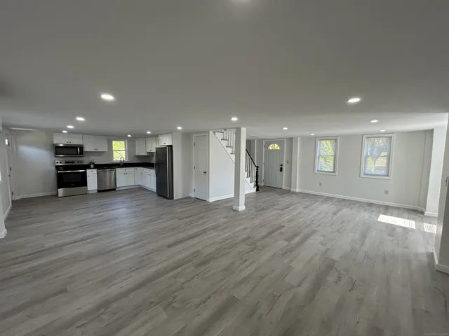 a view of an empty room with wooden floor and a kitchen