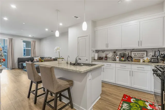 a kitchen with stainless steel appliances granite countertop a sink a stove a refrigerator cabinets and a dining table with wooden floor