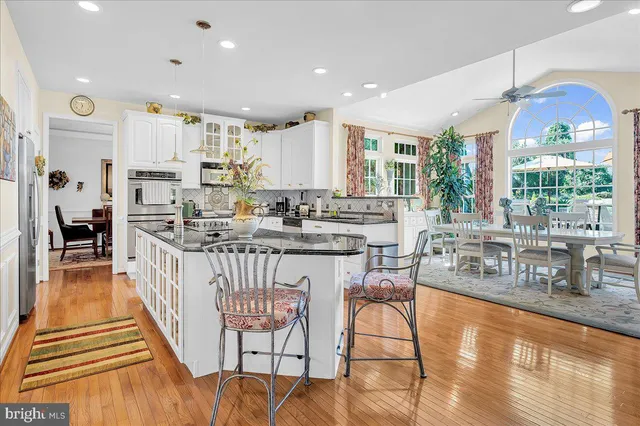 a kitchen with stainless steel appliances granite countertop a stove top oven a sink a dining table and chairs with wooden floor