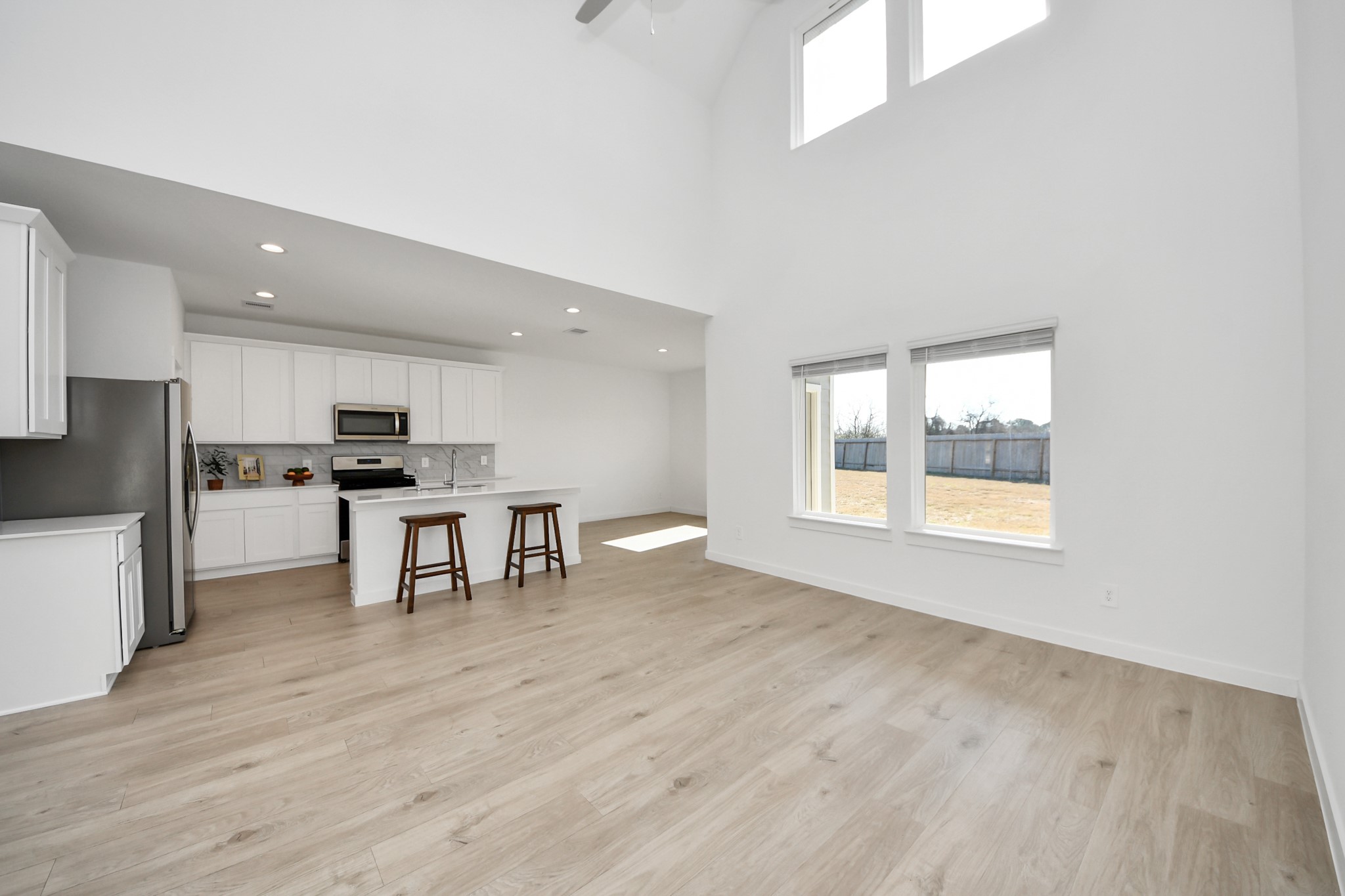 28603 Crowley Court Katy, TX 77494 - Photo 50 of 50 This floor plan showcases a spacious, open living area with high ceilings and abundant natural light. The modern kitchen features white cabinetry, stainless steel appliances, and a central island with seatings. Large windows offer views of a fenced backyard, creating a bright and inviting atmosphere.