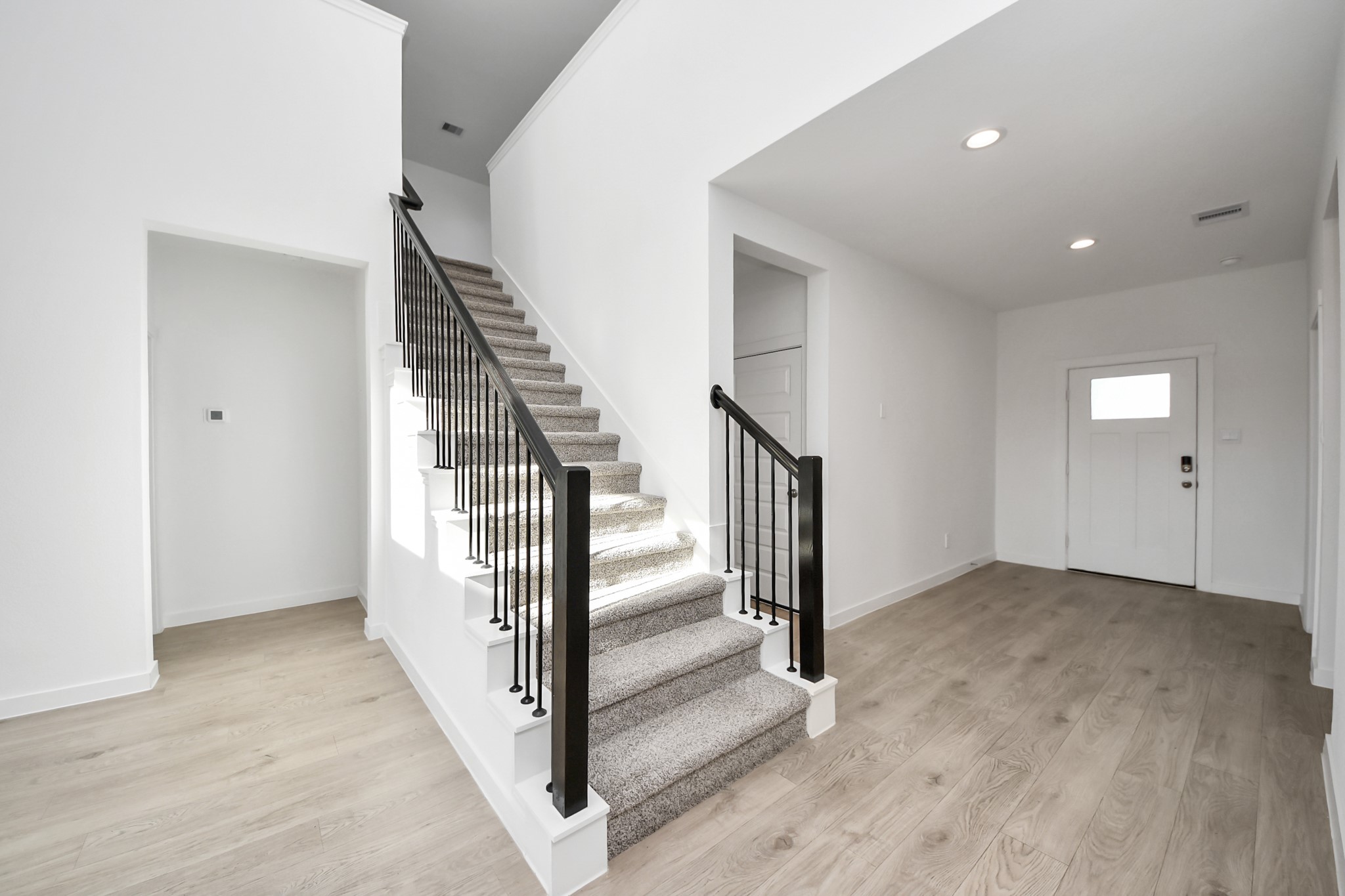 28603 Crowley Court Katy, TX 77494 - Photo 6 of 50 Bright and spacious entryway featuring wood-look flooring and a carpeted staircase with modern black railings. The area is well-lit with recessed lighting and includes a doorway leading to another room.