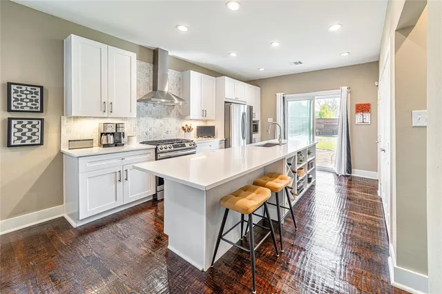a kitchen with stainless steel appliances kitchen island granite countertop a stove a sink a refrigerator and white cabinets with wooden floor