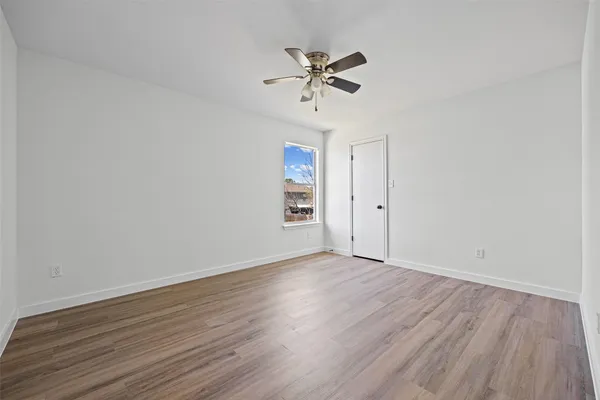 a view of an empty room with wooden floor and a ceiling fan