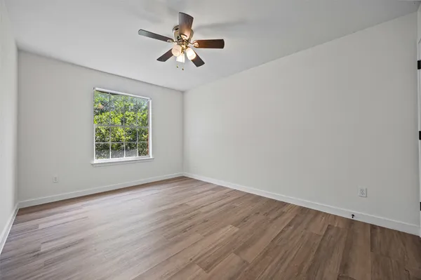 an empty room with wooden floor chandelier fan and windows