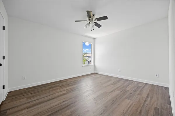 a view of an empty room with wooden floor and a ceiling fan