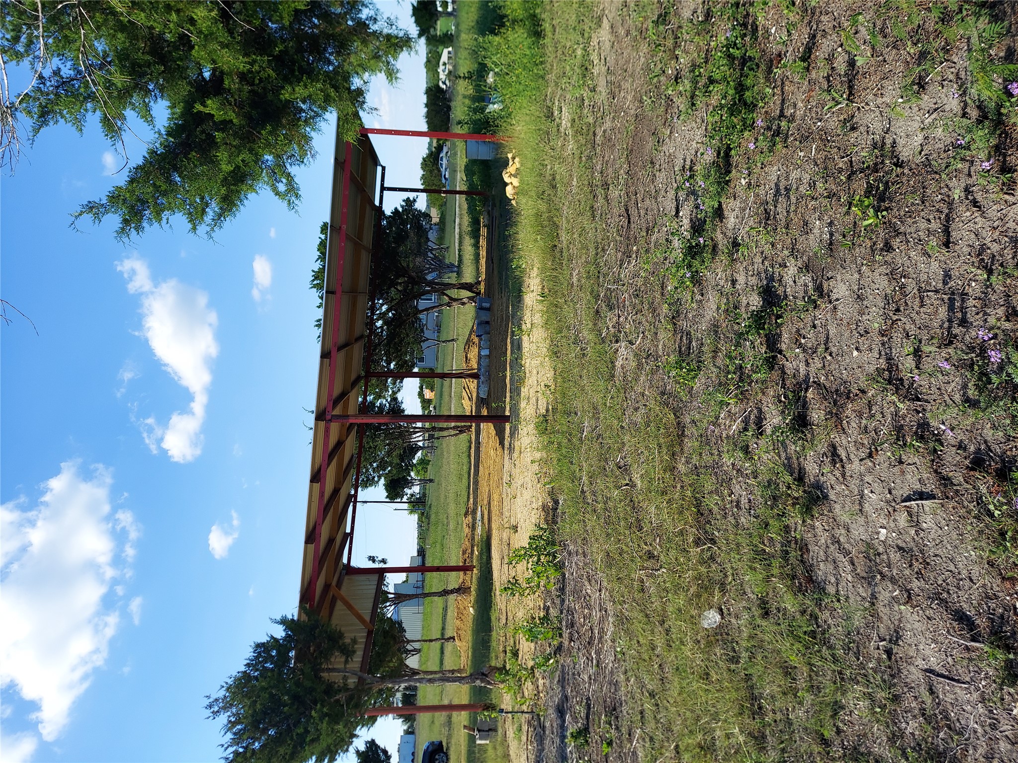 906 County Road 154 Georgetown, TX 78626 - Photo 7 of 11 Open-air metal structure with red-painted support beams and a corrugated roof, situated on a grass and dirt lot