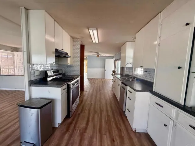 a kitchen with stainless steel appliances a sink a stove top oven a refrigerator a sink dishwasher with wooden floor and cabinets