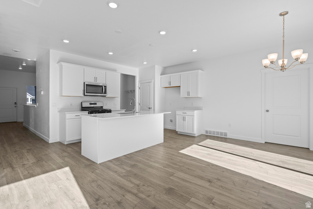 2823 North 710 West, Unit 16 Logan, UT 84321 - Photo 17 of 22 Kitchen featuring white cabinets, suspended lighting, stainless steel appliances, an island with sink, and light wood-type flooring