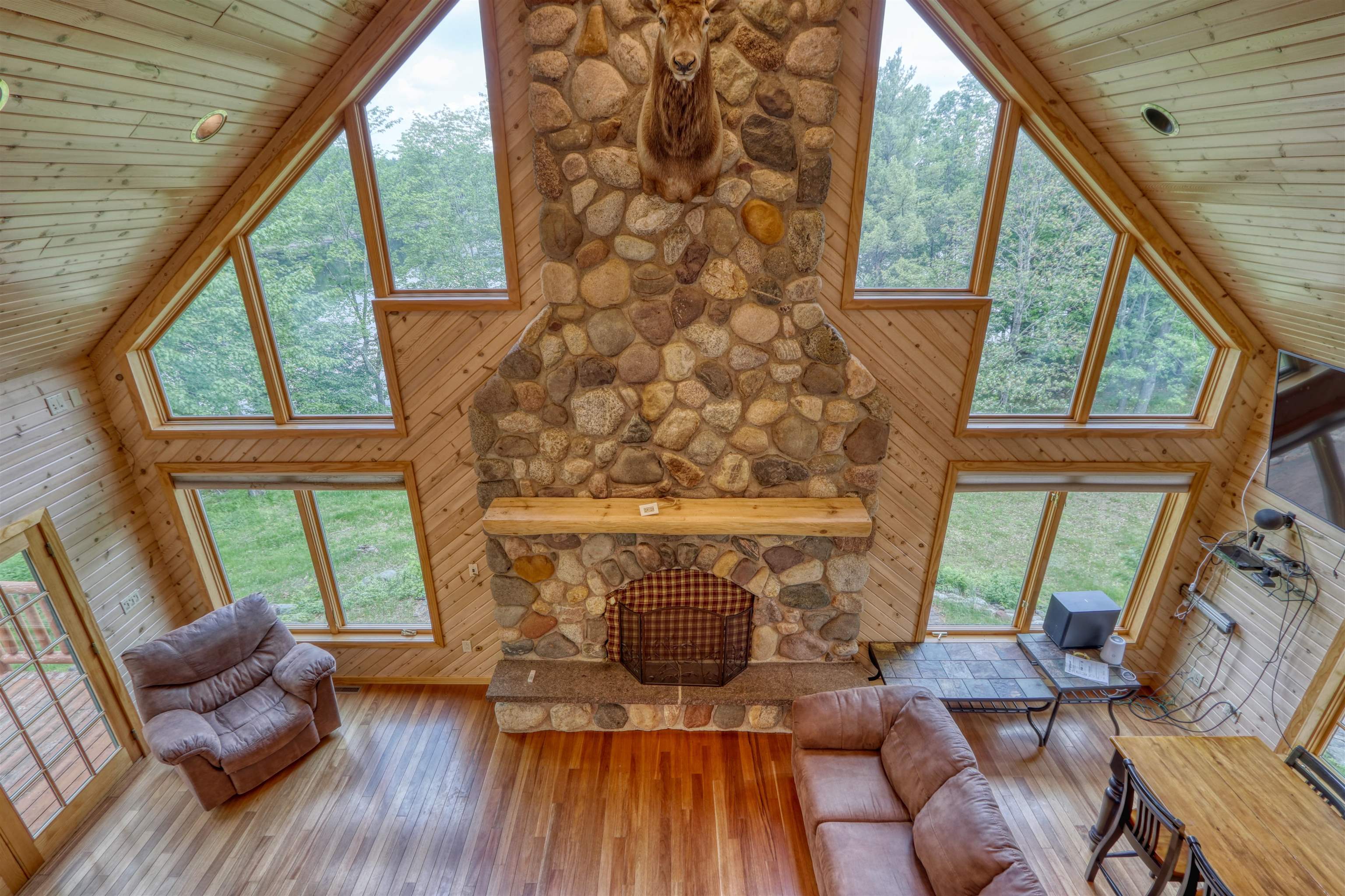 1881 County Road A Spooner, WI 54801 - Photo 18 of 54 Living area with wood ceiling, a stone fireplace, high vaulted ceiling, wood walls, and hardwood / wood-style floors