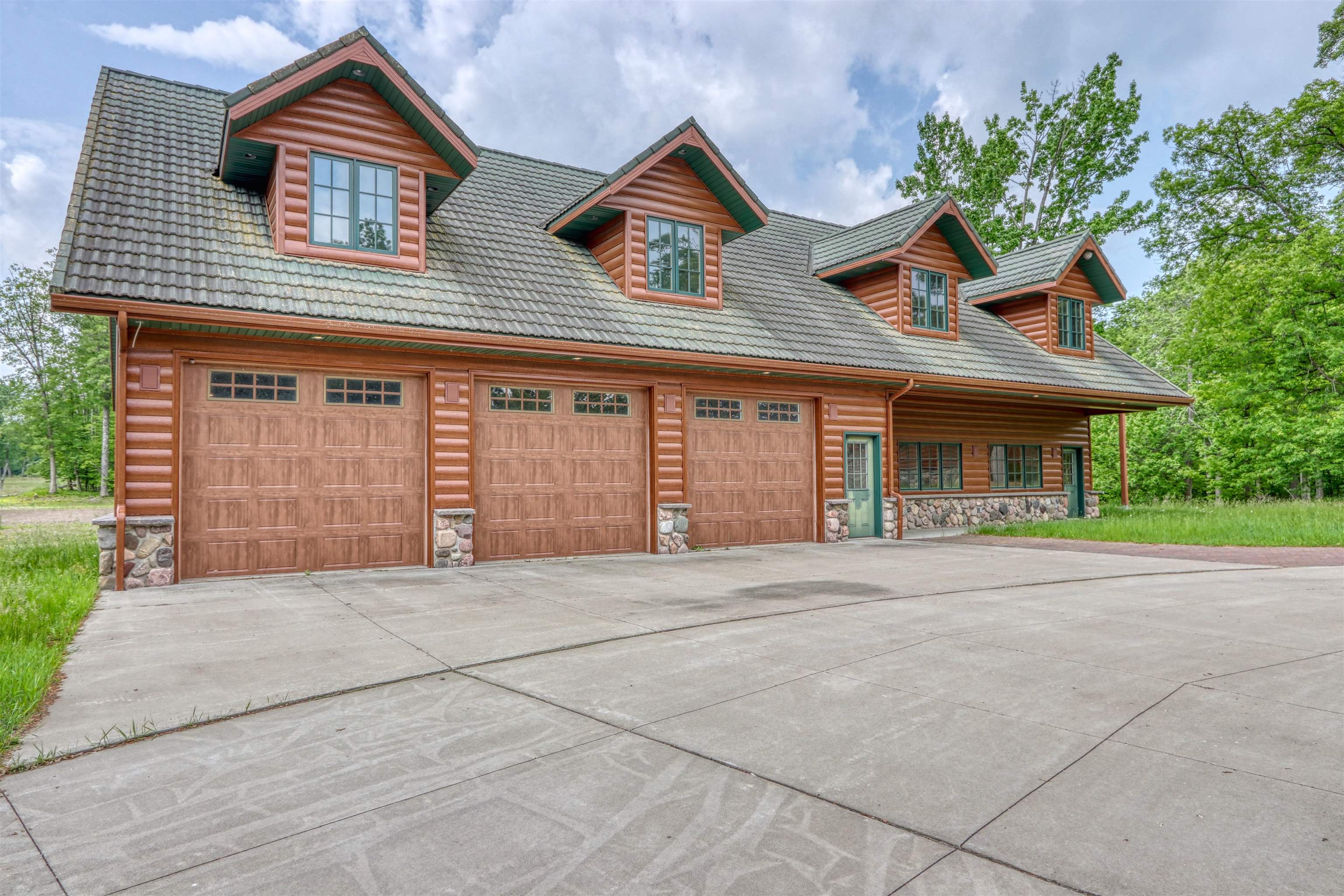 1881 County Road A Spooner, WI 54801 - Photo 49 of 54 Log-style house featuring concrete driveway, stone siding, a porch, and an attached garage