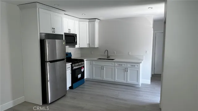 a view of a refrigerator in kitchen and an empty room with wooden floor
