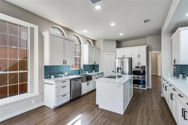 a kitchen with stainless steel appliances a stove top oven a sink a refrigerator white cabinets and wooden floor