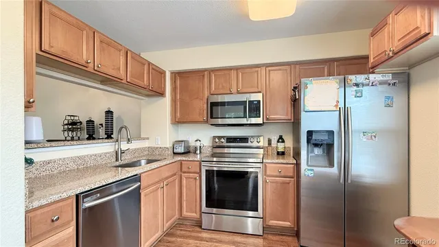 a kitchen with stainless steel appliances granite countertop a refrigerator a stove a sink and dishwasher with wooden floor