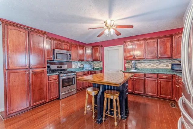 a kitchen with stainless steel appliances kitchen island granite countertop wooden floors and wooden cabinets