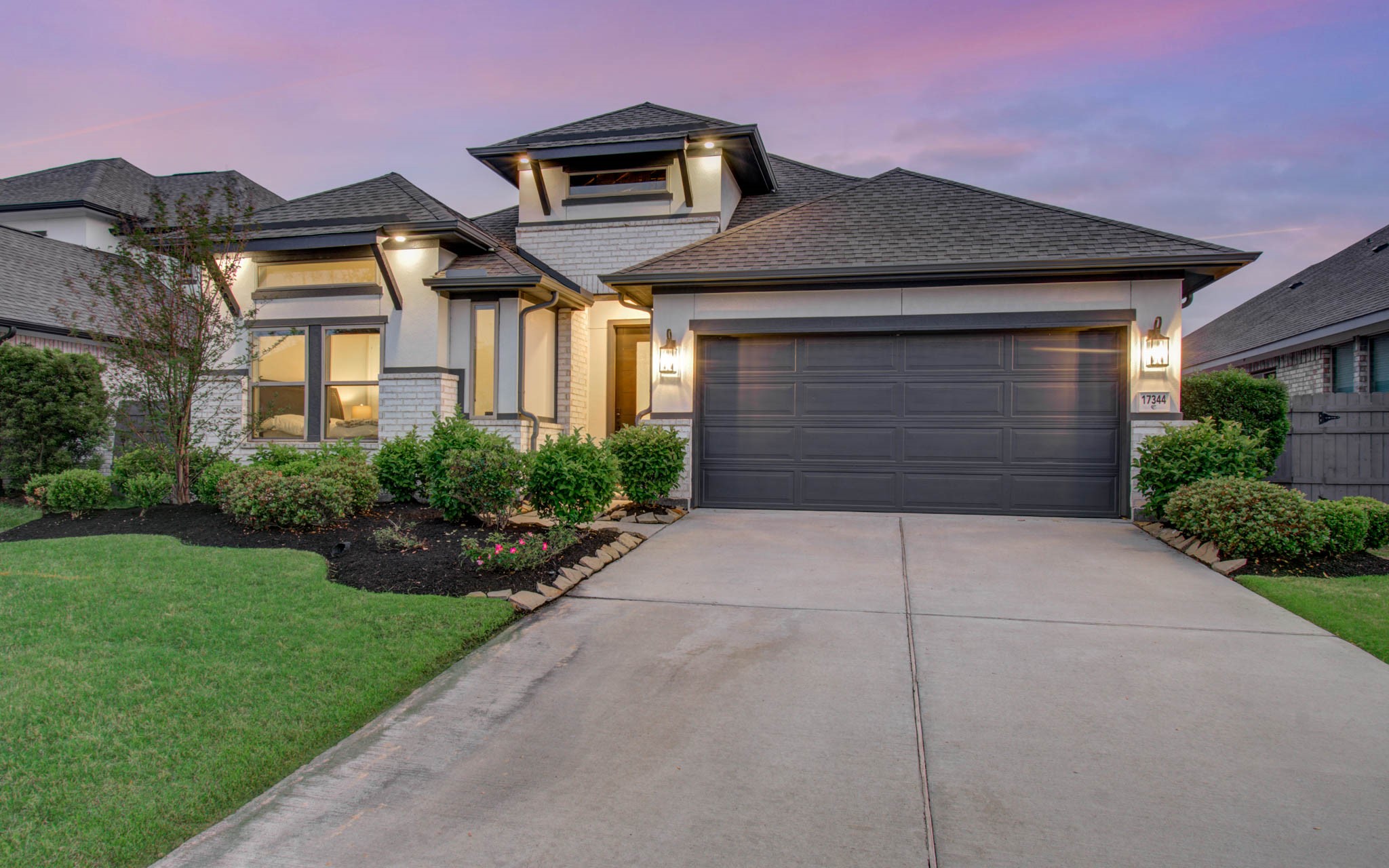 17344 Grand Canyon Road Conroe, TX 77302 - Photo 1 of 49 This modern home features a stylish exterior with a two-car garage, well-maintained landscaping, and elegant lighting. The driveway is spacious, and the overall curb appeal is enhanced by a serene evening sky.