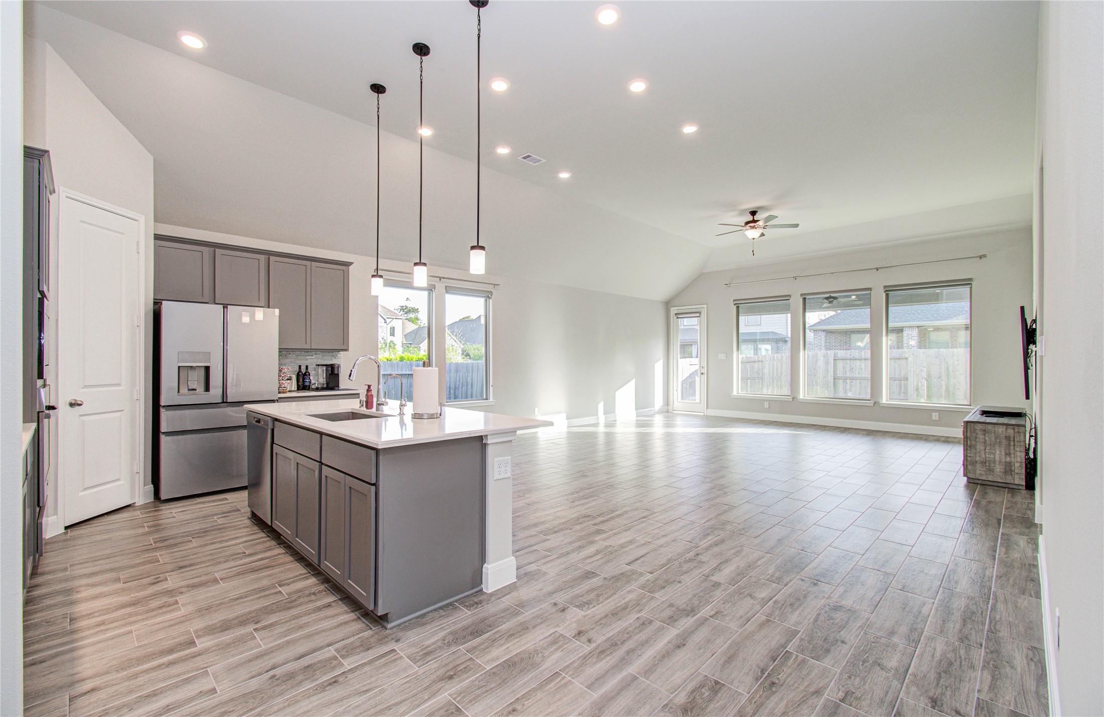 17344 Grand Canyon Road Conroe, TX 77302 - Photo 15 of 49 This photo showcases a spacious, open-concept living area with high ceilings, abundant natural light from large windows, and modern finishes. The kitchen features a central island, stainless steel appliances, and ample cabinet space, while the living area offers sleek tile flooring and a ceiling fan.