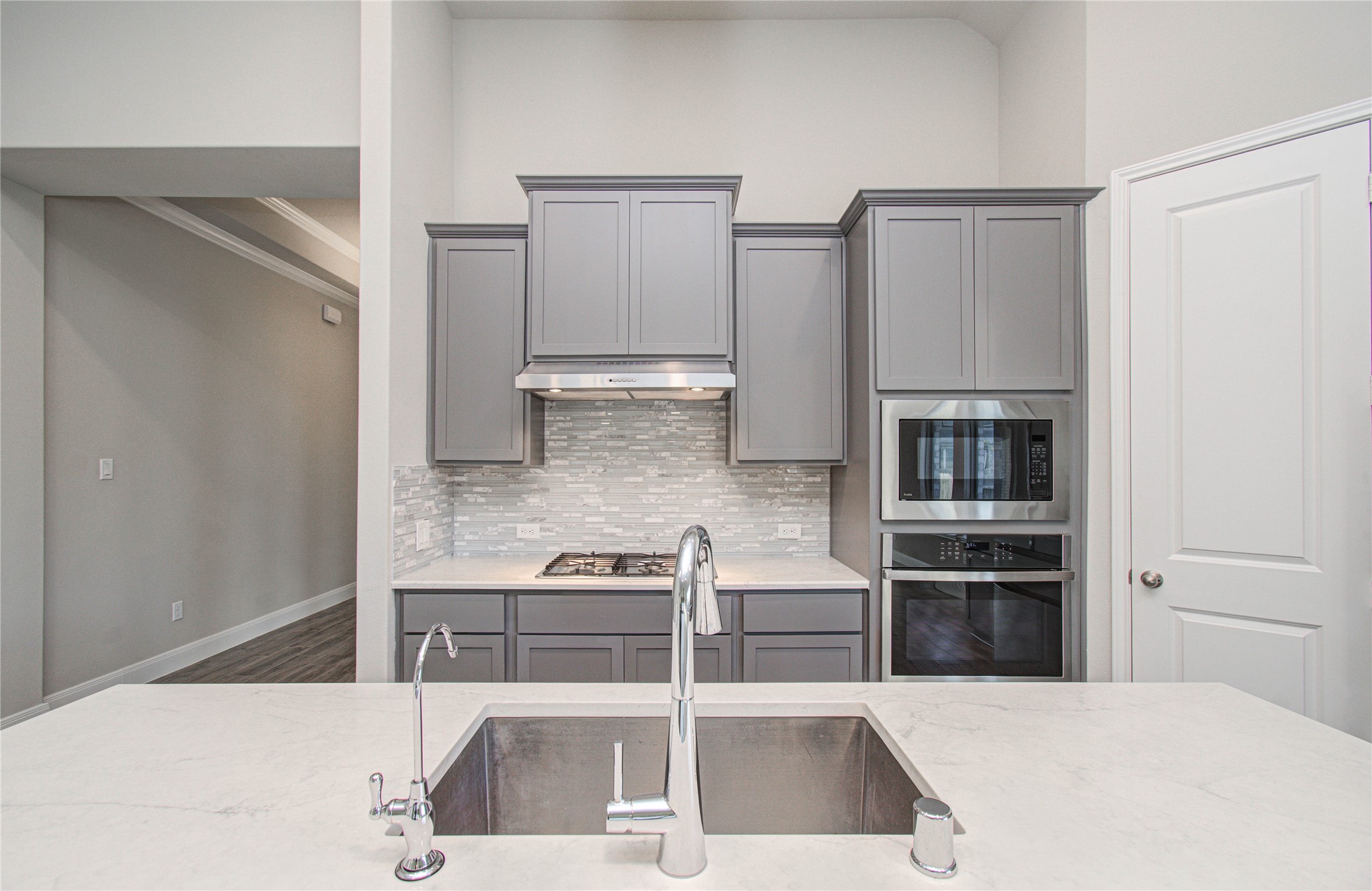 17344 Grand Canyon Road Conroe, TX 77302 - Photo 18 of 49 This modern kitchen features sleek gray cabinetry, a stylish tile backsplash, and stainless steel appliances, including a built-in microwave and oven. The spacious island with a sink and quartz contertops, offers ample workspace and a contemporary feel.