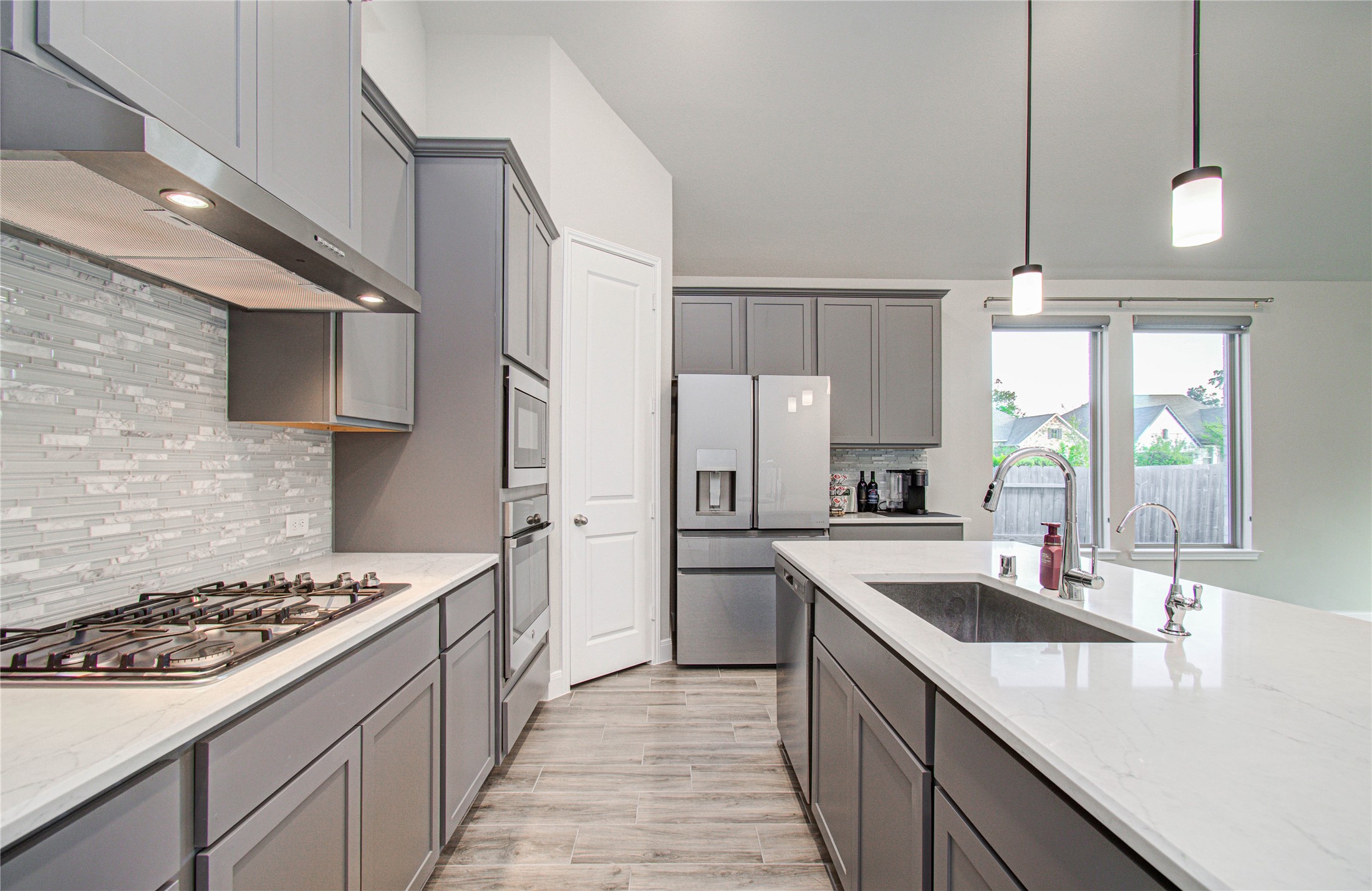 17344 Grand Canyon Road Conroe, TX 77302 - Photo 19 of 49 This modern kitchen features sleek gray cabinetry, a stylish tile backsplash, and stainless steel appliances. It includes a spacious quartz contertops, island with a sink and pendant lighting, offering a bright and functional space ideal for cooking and entertaining. Large windows provide ample natural light.
