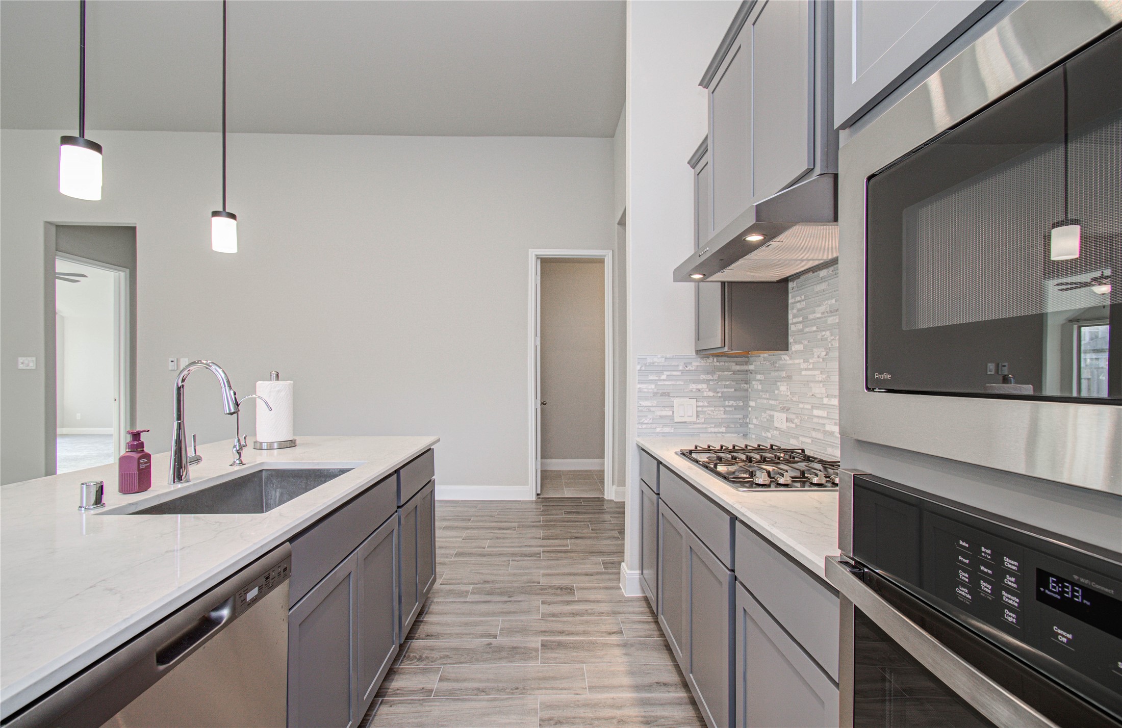 17344 Grand Canyon Road Conroe, TX 77302 - Photo 20 of 49 Modern kitchen featuring sleek gray cabinetry, stainless steel appliances, and a spacious island with a sink. Elegant pendant lighting and a stylish tile backsplash enhance the contemporary design.