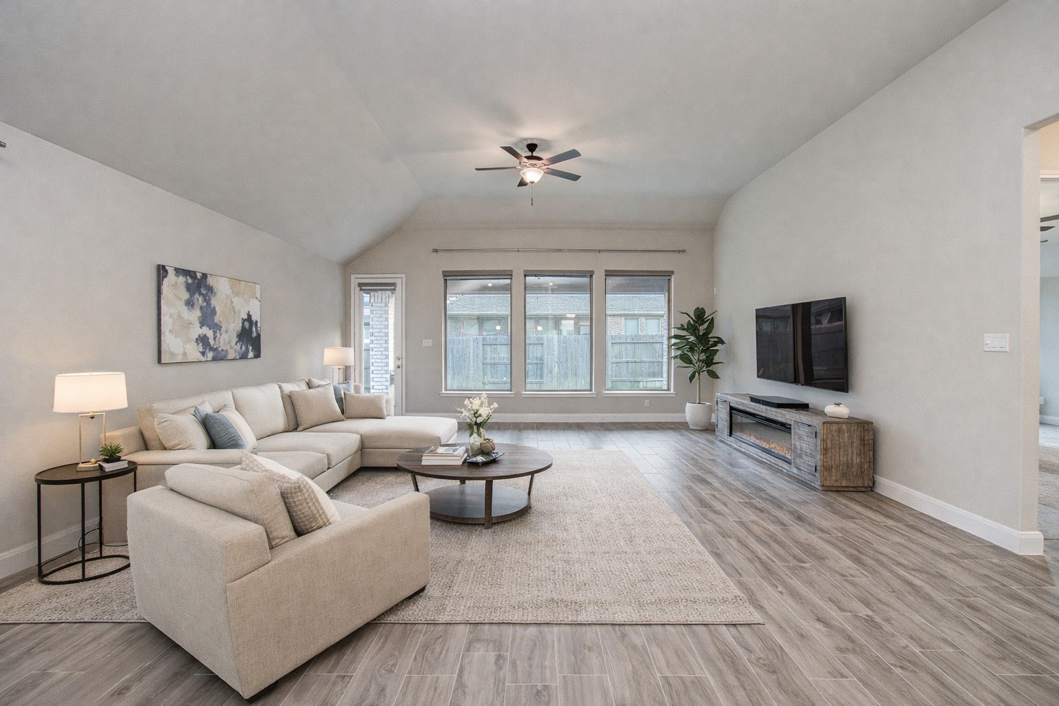 17344 Grand Canyon Road Conroe, TX 77302 - Photo 32 of 49 This spacious living room features a vaulted ceiling with a ceiling fan, large windows for natural light, and wood-look flooring. It includes a comfortable sectional sofa, modern decor, and a wall-mounted TV above a stylish console.