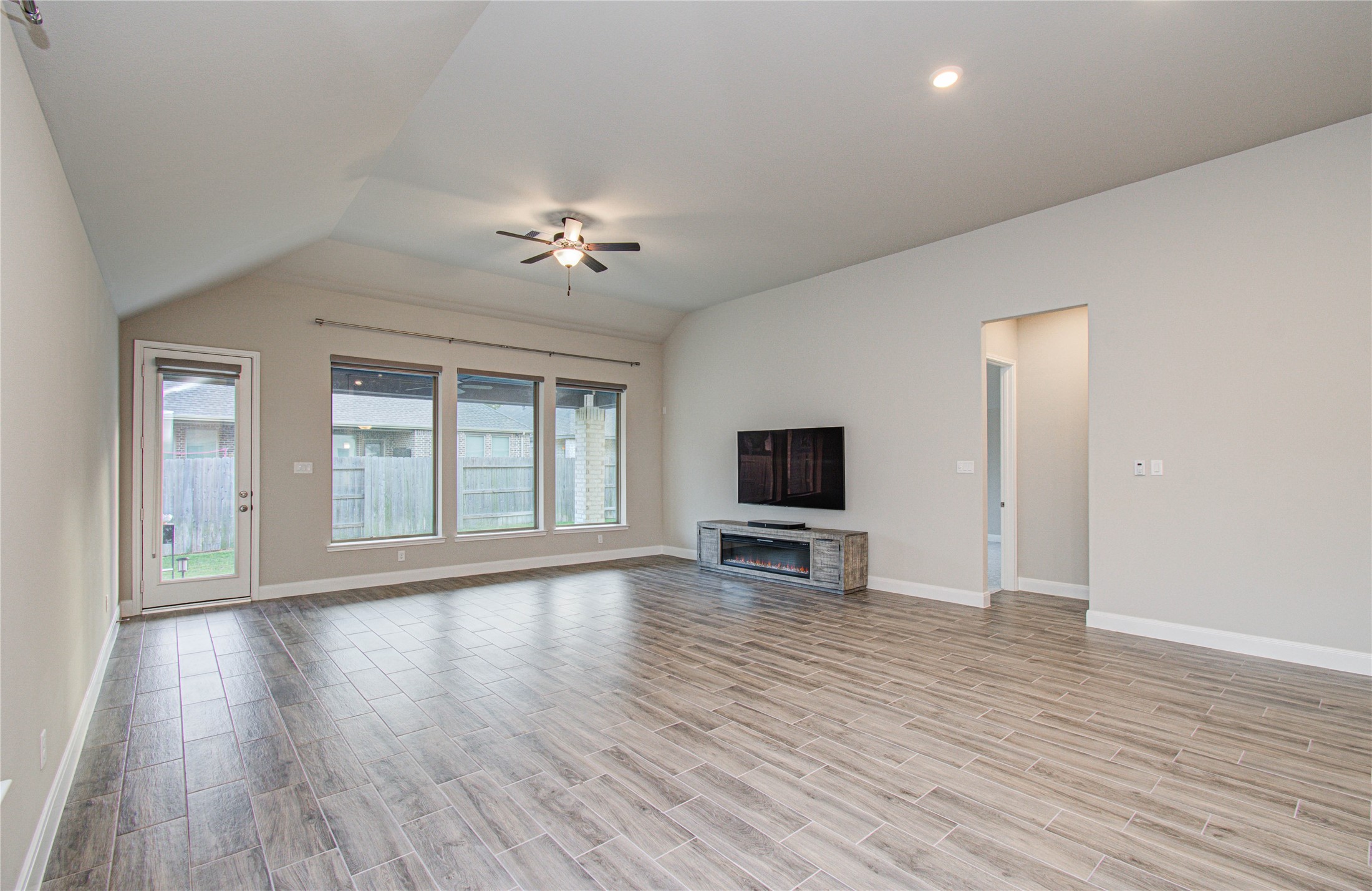 17344 Grand Canyon Road Conroe, TX 77302 - Photo 33 of 49 This spacious living room features large windows for natural light, a ceiling fan, and modern wood-look tile flooring. It includes a mounted TV and an electric fireplace, with access to the backyard through a glass door.
