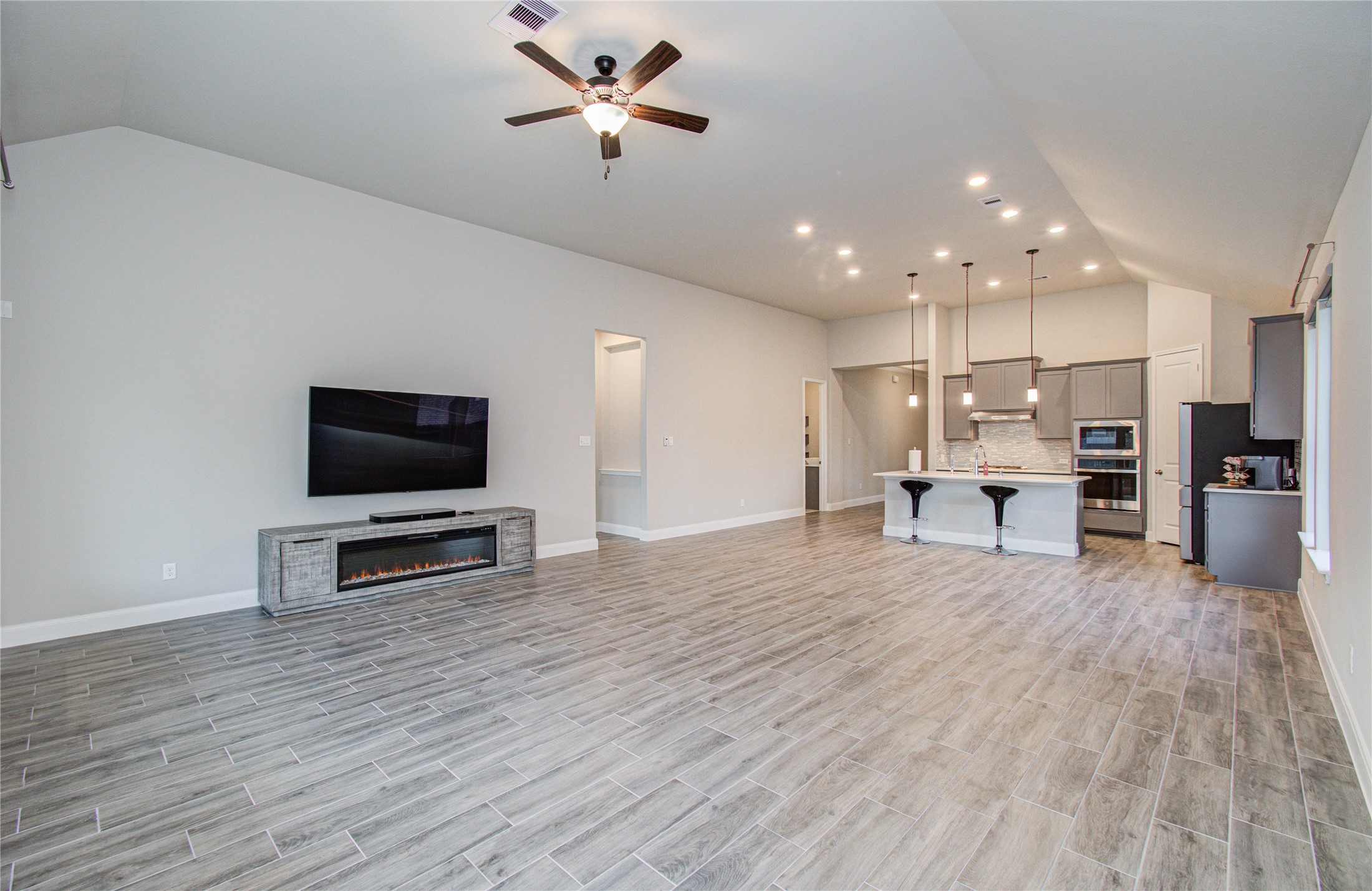 17344 Grand Canyon Road Conroe, TX 77302 - Photo 35 of 49 Spacious open-concept living area with modern tile flooring, high ceilings, and recessed lighting. The room features a mounted TV and a sleek electric fireplace. The kitchen boasts an island with bar seating, pendant lighting, and contemporary cabinetry.