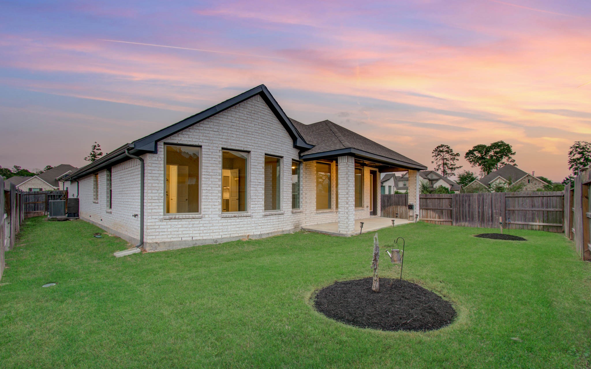 17344 Grand Canyon Road Conroe, TX 77302 - Photo 43 of 49 This image shows a charming single-story brick home with a spacious, fenced backyard. The well-maintained lawn features small landscaped areas, and a covered patio offers outdoor relaxation space. The sunset sky adds to the inviting atmosphere.