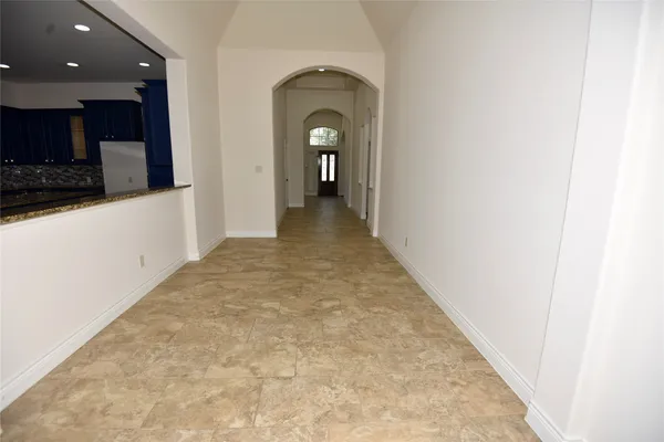 a view of a hallway to an empty room and kitchen