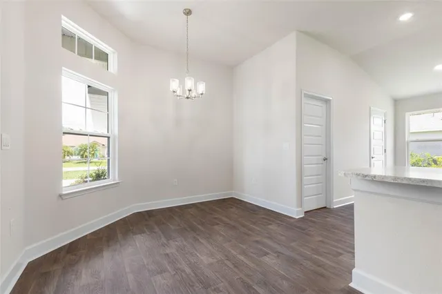 an empty room with wooden floor chandelier and windows